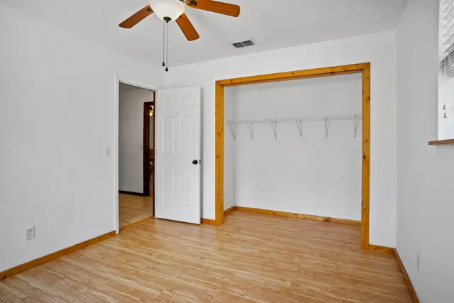 a view of an empty room with wooden floor and a ceiling fan