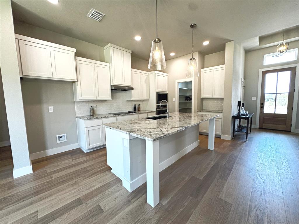 1005 Ronnie Court Springtown, TX 76082 - Photo 10 of 27 Kitchen featuring a large central island with a light-toned countertop, white cabinetry, integrated stainless steel appliances, a tiled backsplash, and wood-finish flooring