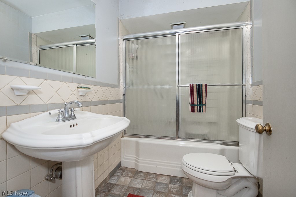 4541 Emerson Road Cleveland, OH 44121 - Photo 6 of 12 Bathroom featuring tile walls, tile flooring, combined bath / shower with glass door, and toilet