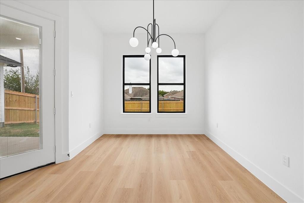 1652 West Wintergreen Road Lancaster, TX 75134 - Photo 13 of 25 Wood-finish flooring throughout, bright white walls, modern chandelier, two black-framed windows, and a glass-paneled door