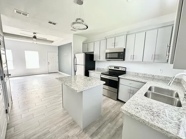 a kitchen with granite countertop a stove top oven a sink a refrigerator and white cabinets