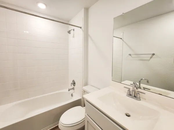 a bathroom with a bathtub shower sink vanity mirror and toilet