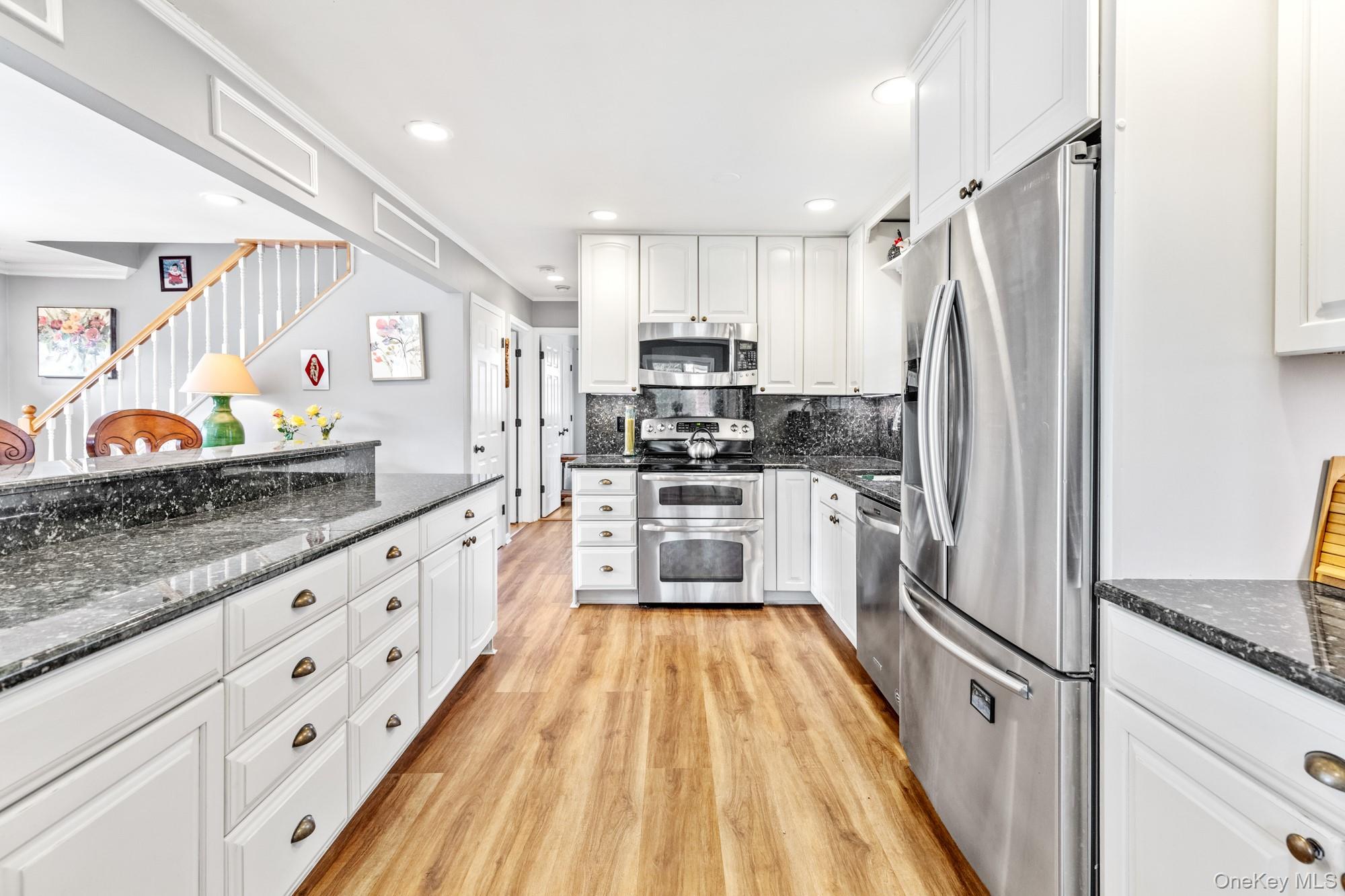 79 East Tiana Road Hampton Bays, NY 11946 - Photo 14 of 26 a large white kitchen with stainless steel appliances granite countertop a lot of counter space and wooden floor