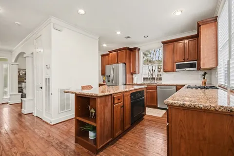 a kitchen with stainless steel appliances granite countertop wooden cabinets a sink dishwasher a stove and a refrigerator with wooden floor