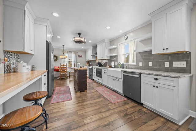 a kitchen with stainless steel appliances kitchen island granite countertop a refrigerator a sink dishwasher and white cabinets with wooden floor