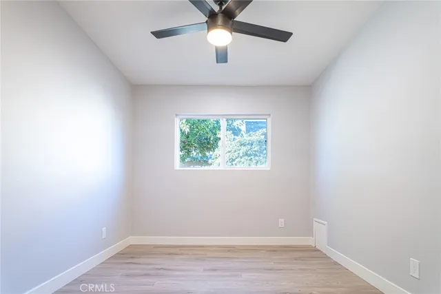 an empty room with wooden floor ceiling fan and window