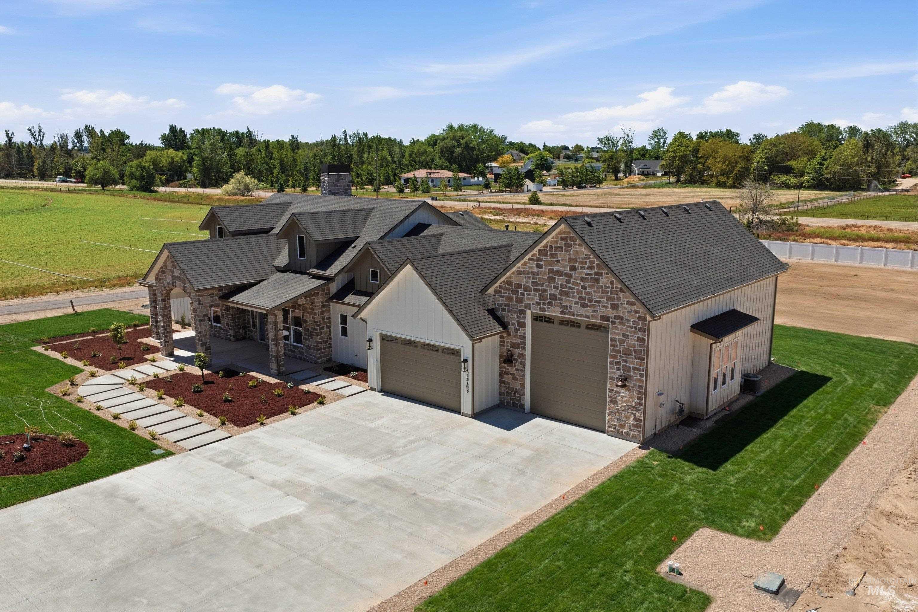 24821 Ardmore Court Caldwell, ID 83607 - Photo 3 of 43 Contemporary-style exterior featuring stone and board-and-batten siding, a multi-car garage, expansive concrete driveway, and newly installed landscaping with mature trees