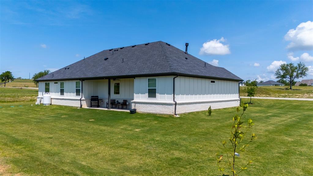 2004 Willy Dilly Road Springtown, TX 76082 - Photo 34 of 40 Expansive rear exterior featuring a covered patio, a manicured lawn, white vertical siding, and a dark shingle roof