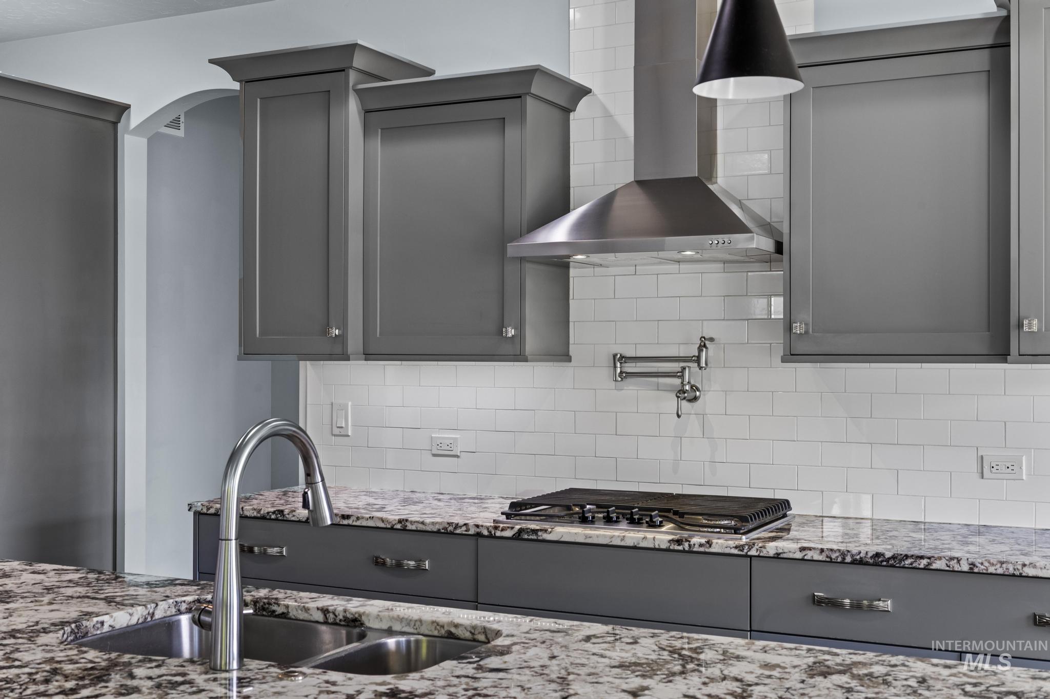 2681 East Rhyolite Court Nampa, ID 83686 - Photo 14 of 48 Gourmet kitchen featuring a stainless steel range hood, white subway tile backsplash, gray cabinetry, granite countertops, and a dual basin sink with a gooseneck faucet