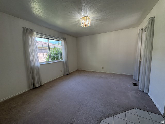 486 West 120 North Orem, UT 84057 - Photo 5 of 30 Spacious room featuring neutral carpeting, a large window with natural lighting, textured ceiling, and a decorative ceiling light fixture
