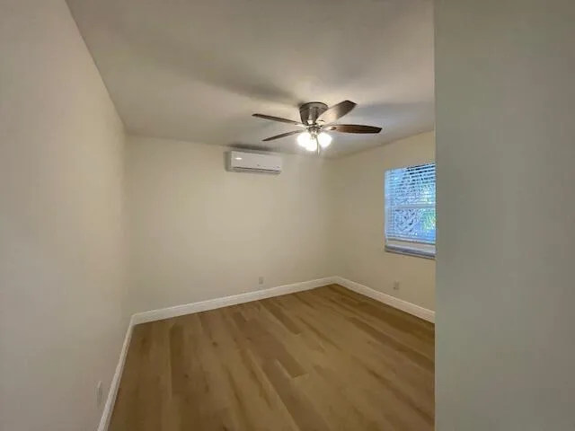 an empty room with a chandelier fan and wooden floor