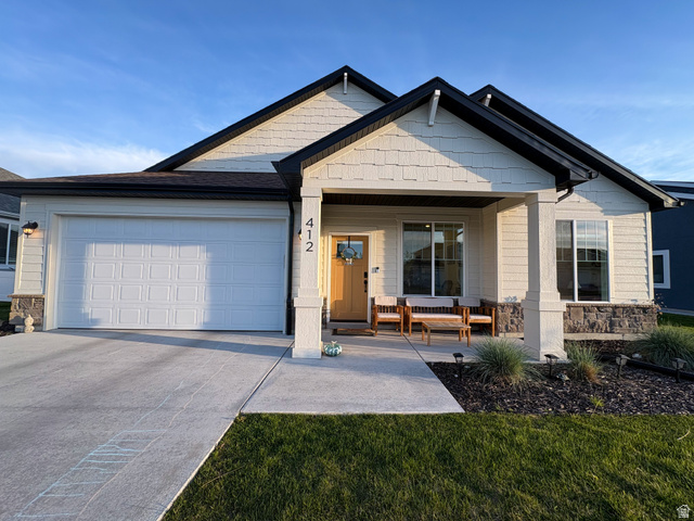 View of front of house featuring stone siding, a garage, a porch, and concrete driveway