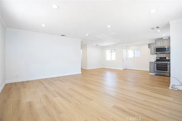 an empty room with wooden floor and kitchen view