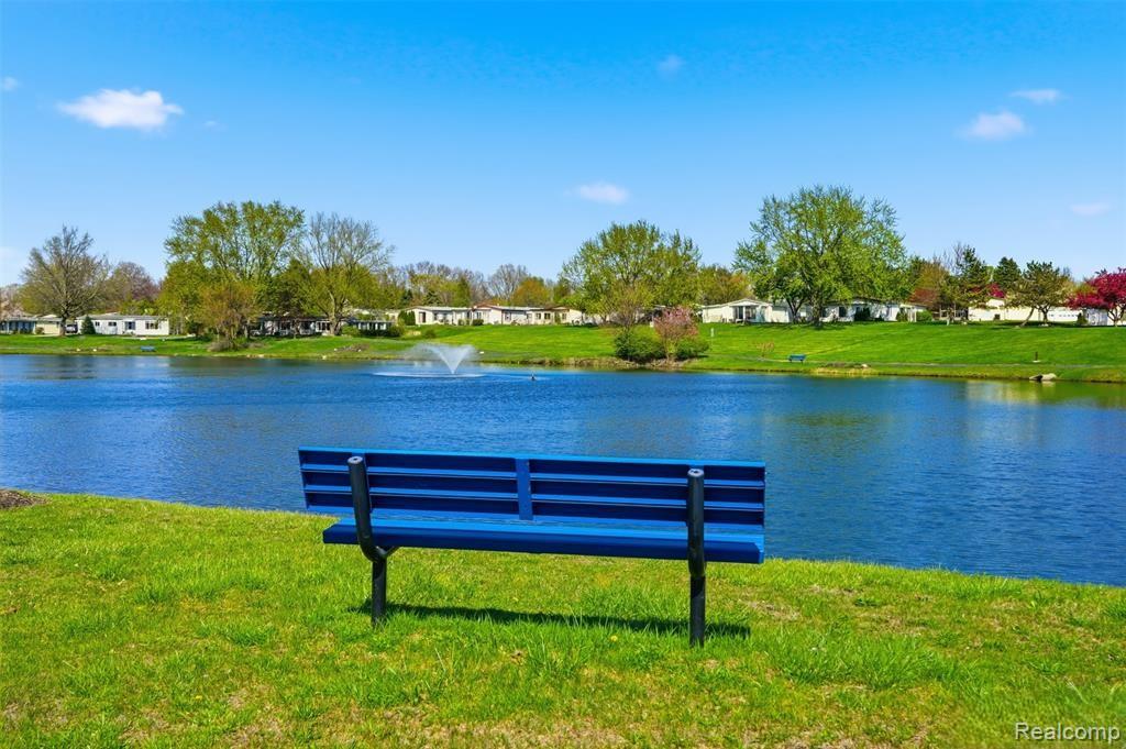 150 Whippoorwill Lane Rochester, MI 48309 - Photo 27 of 28 Blue park bench positioned on a grassy bank overlooking a body of water