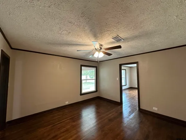 an empty room with wooden floor chandelier fan and windows