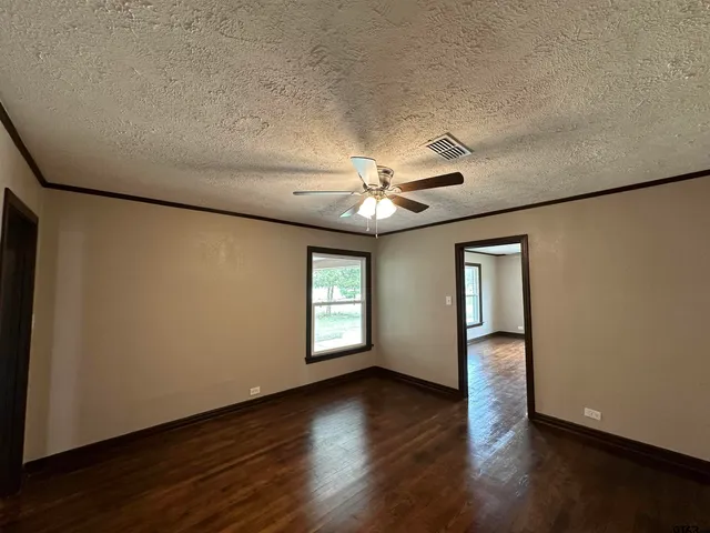 an empty room with wooden floor chandelier fan and windows