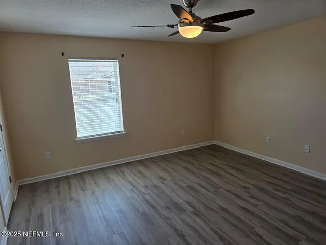 an empty room with wooden floor fan and windows