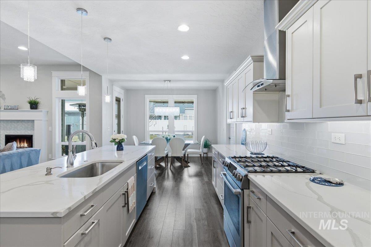 5154 South Twilight Mist Way Meridian, ID 83642 - Photo 16 of 47 Kitchen with stainless steel appliances, a lit fireplace, dark wood finished floors, light stone counters, and decorative light fixtures