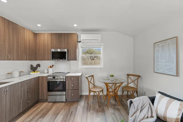 a open kitchen with stainless steel appliances granite countertop a stove top oven a sink dishwasher a dining table and chairs with wooden floor