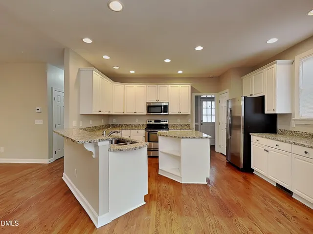 a kitchen with stainless steel appliances kitchen island granite countertop a stove top oven a sink a refrigerator and white cabinets with wooden floor