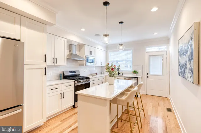 a kitchen with stainless steel appliances kitchen island a refrigerator a stove a sink dishwasher and a dining table with wooden floor