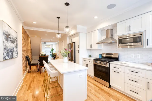 a kitchen with stainless steel appliances kitchen island granite countertop a stove a sink a oven a dining table and chairs with wooden floor