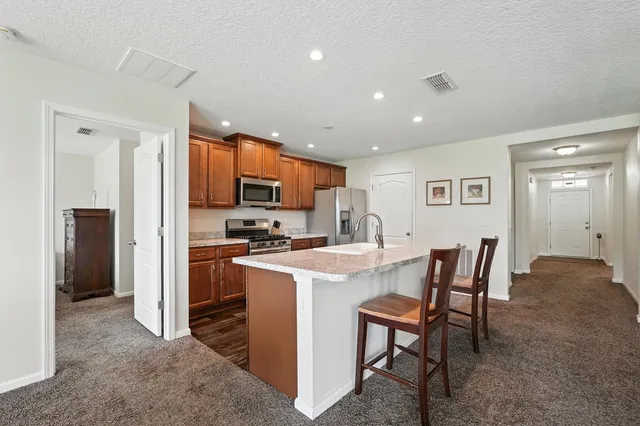 a kitchen with stainless steel appliances granite countertop a refrigerator a stove a sink a dining table and chairs with wooden floor