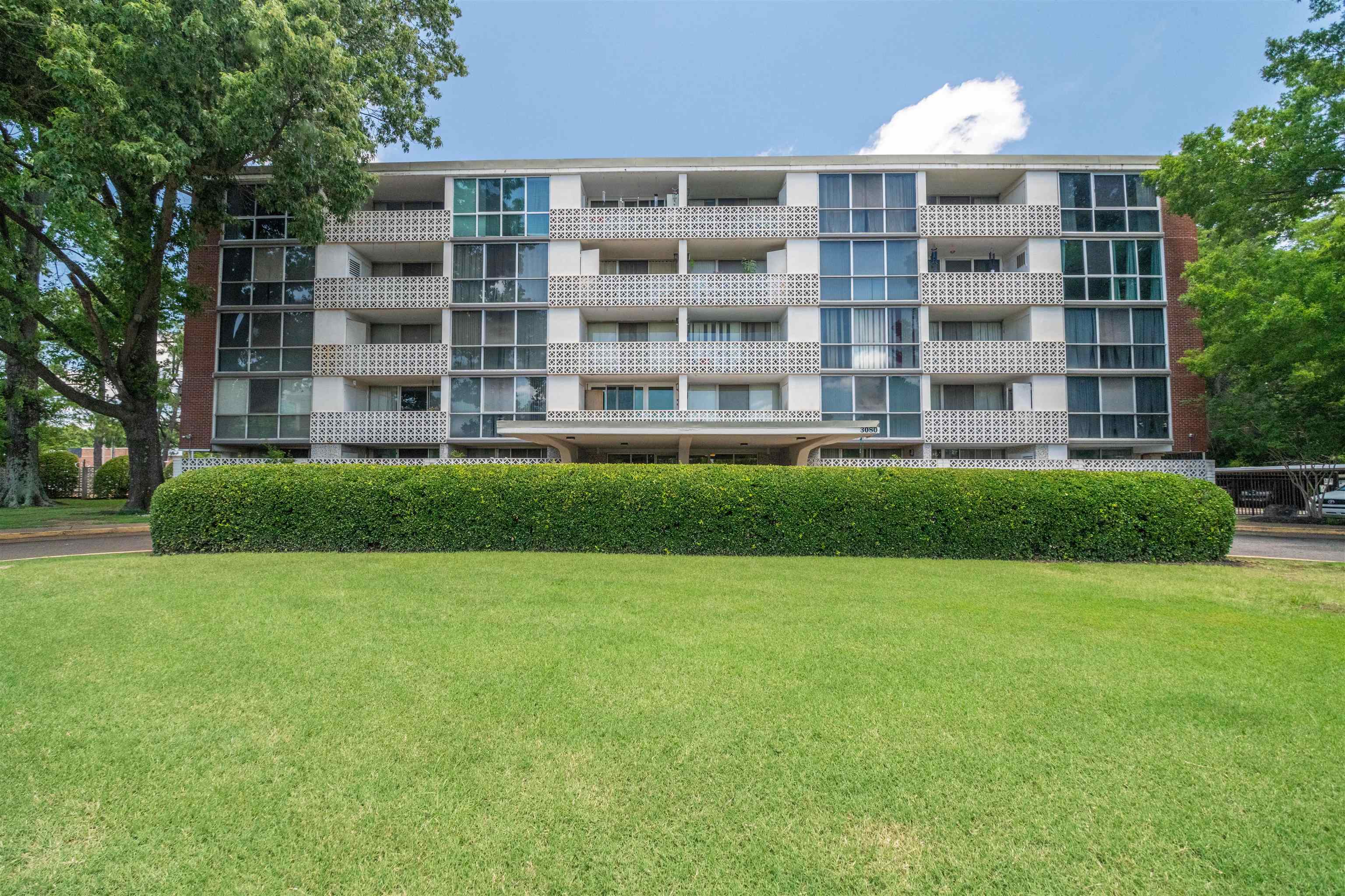 3080 Walnut Grove Road, Unit 306 Memphis, TN 38111 - Photo 18 of 18 Multi-story building featuring brick and white paneling, individual balconies with decorative screens, a prominent covered entrance, and a well-maintained foreground lawn with mature hedges