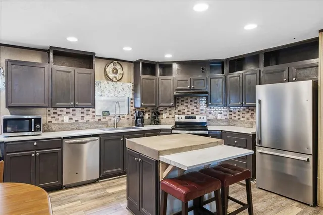 a kitchen with stainless steel appliances a sink a stove a refrigerator cabinets and chairs