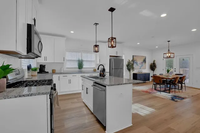 a kitchen with stainless steel appliances kitchen island granite countertop a sink a stove and a wooden floors