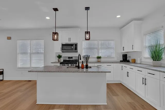 a kitchen with stainless steel appliances granite countertop a sink a window and white cabinets