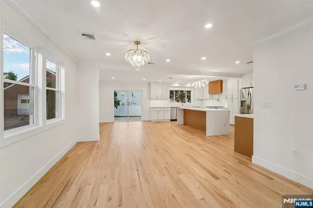 a view of an empty room and kitchen with wooden floor