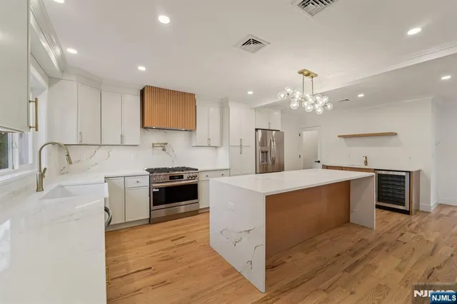 a large kitchen with stainless steel appliances a stove top oven a sink dishwasher and a refrigerator with wooden floor