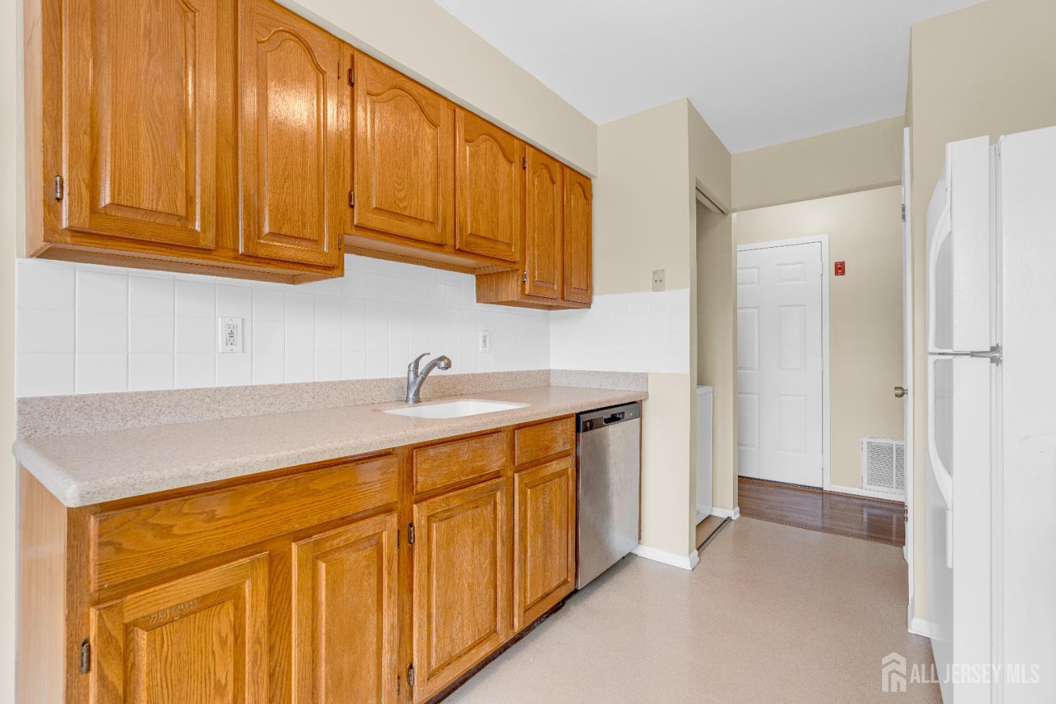 101 Beverly Hl Terrace, Unit M Woodbridge, NJ 07095 - Photo 12 of 28 a hallway with stainless steel appliances granite countertop a sink dishwasher and a refrigerator with wooden cabinets
