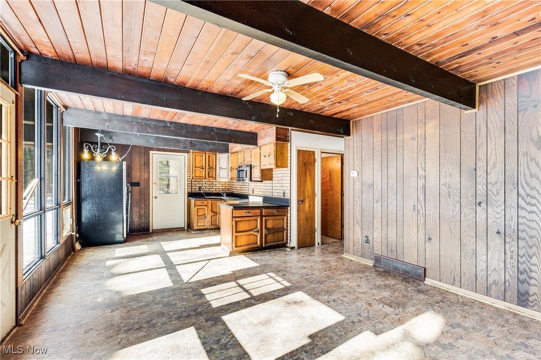 Kitchen with wooden walls, dark countertops, wood finish cabinets, a wooden ceiling with exposed beams, and tasteful backsplash