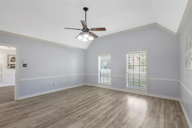 an empty room with wooden floor fan and windows