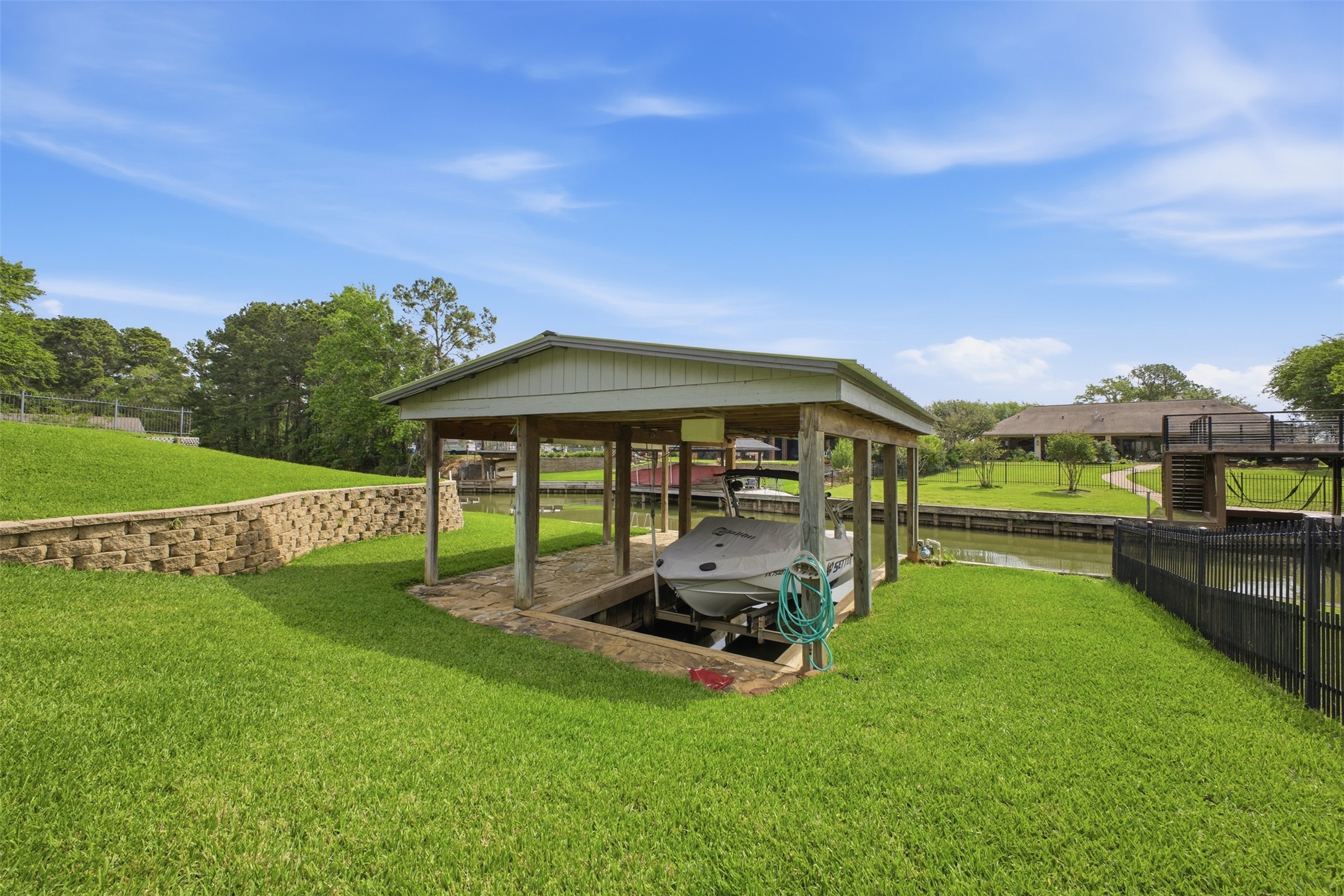 12710 Aries Loop Willis, TX 77318 - Photo 38 of 40 The property features a boat house with a covered slip, a lush green lawn, and a stone retaining wall