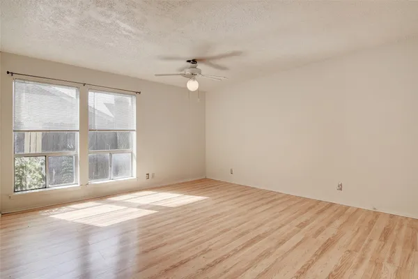 an empty room with wooden floor fan and windows
