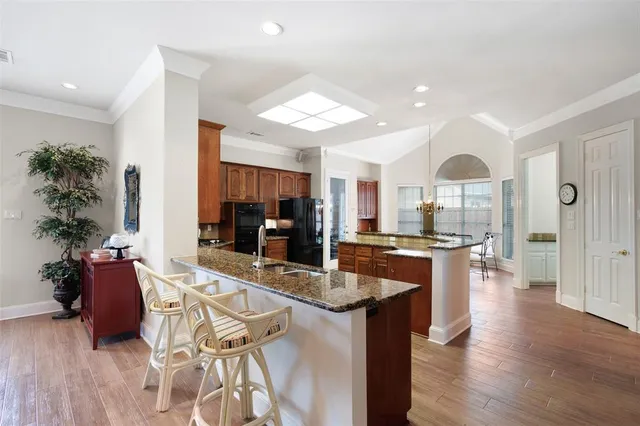 a kitchen with stainless steel appliances kitchen island granite countertop a stove a refrigerator a sink a dining table and chairs with wooden floor
