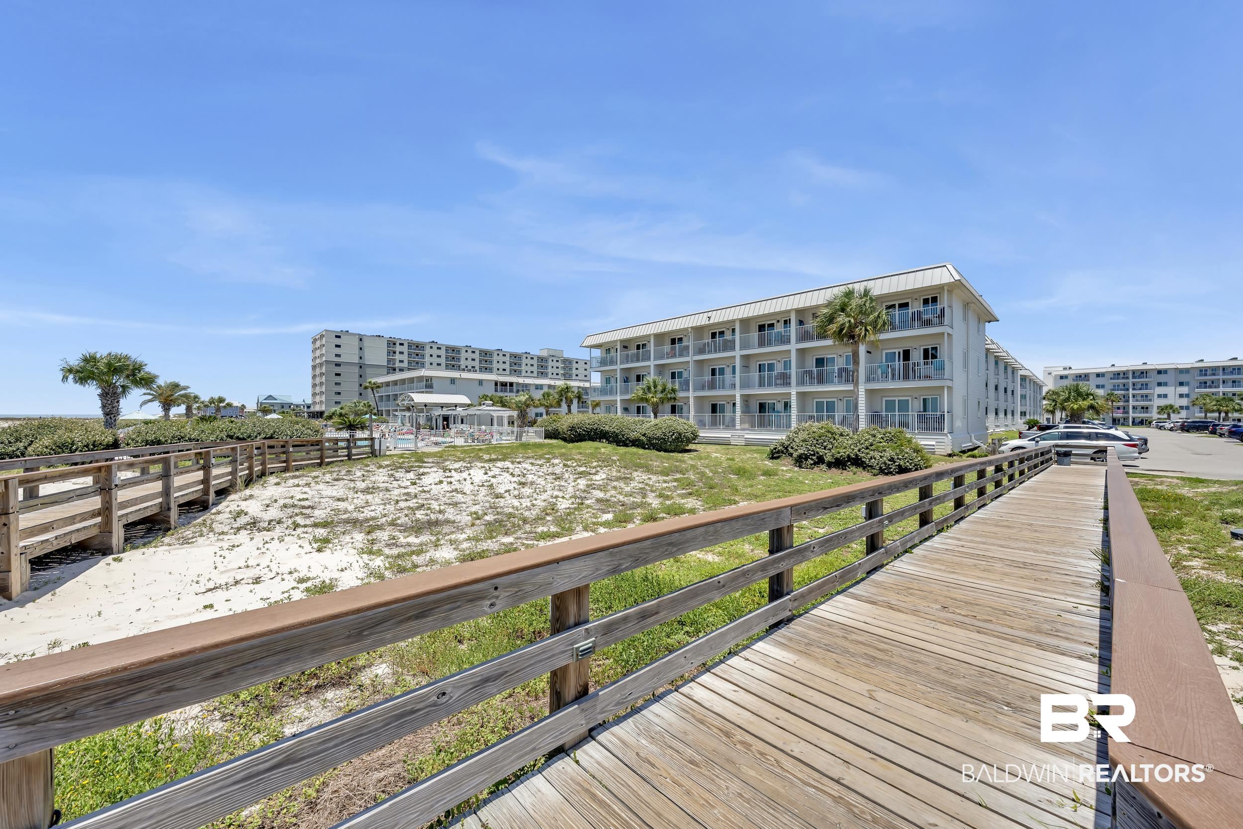 400 Plantation Road, Unit 2118 Gulf Shores, AL 36542 - Photo 38 of 59 Coastal property featuring a boardwalk entrance, sandy grounds, lush green landscaping, a resort-style building with multiple balconies, and a parking area