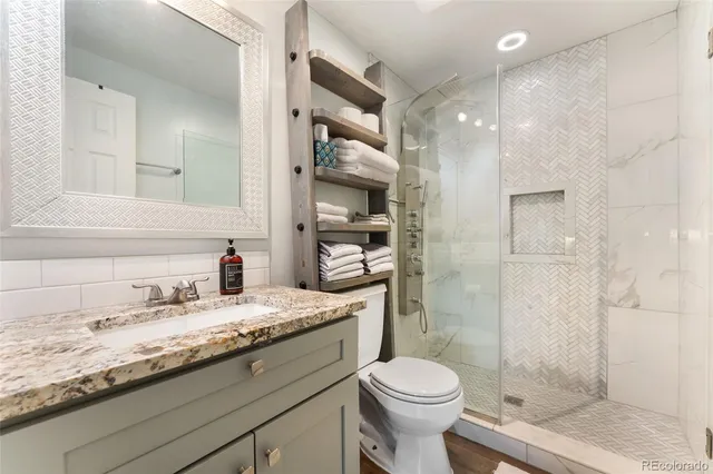 a bathroom with a granite countertop sink a toilet a mirror and shower