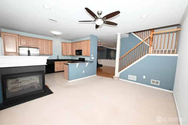 a living room with stainless steel appliances kitchen island granite countertop a refrigerator a stove a sink dishwasher and a fireplace with wooden floor