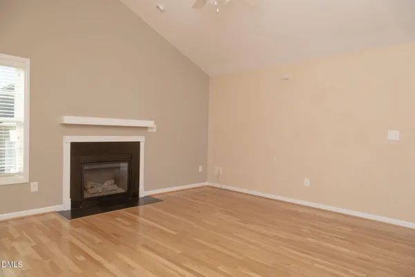 a view of an empty room with wooden floor and a fireplace