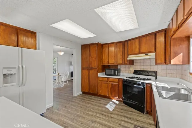 a kitchen with stainless steel appliances granite countertop wooden cabinets a refrigerator a stove a sink and dishwasher with wooden floor