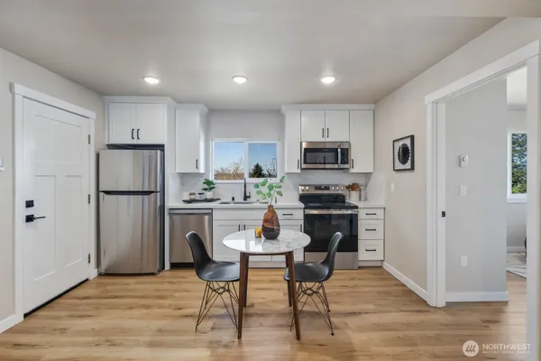 a kitchen with a refrigerator a stove top oven a sink dishwasher a dining table and chairs with wooden floor