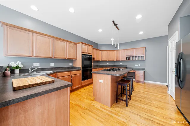 a kitchen with stainless steel appliances granite countertop a refrigerator a sink dishwasher a stove top oven a large island with chairs and wooden floor