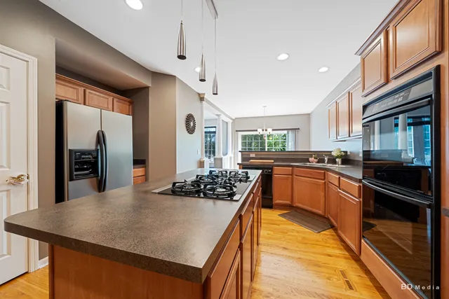 a kitchen with stainless steel appliances kitchen island granite countertop a refrigerator a stove and a sink with wooden floor