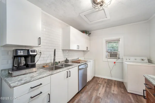 a kitchen with a sink dishwasher and white cabinets with wooden floor