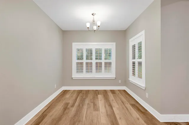 an empty room with wooden floor chandelier and windows