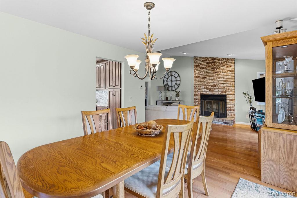 8742 Hyne Road Brighton, MI 48114 - Photo 16 of 65 Dining room featuring light wood-style flooring, a fireplace, and a chandelier
